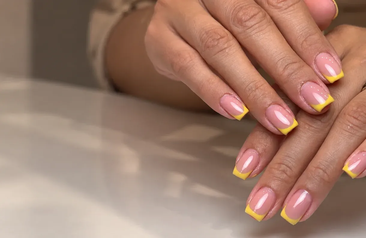 Manos con manicura rosa y puntas amarillas sobre una mesa del estudio.