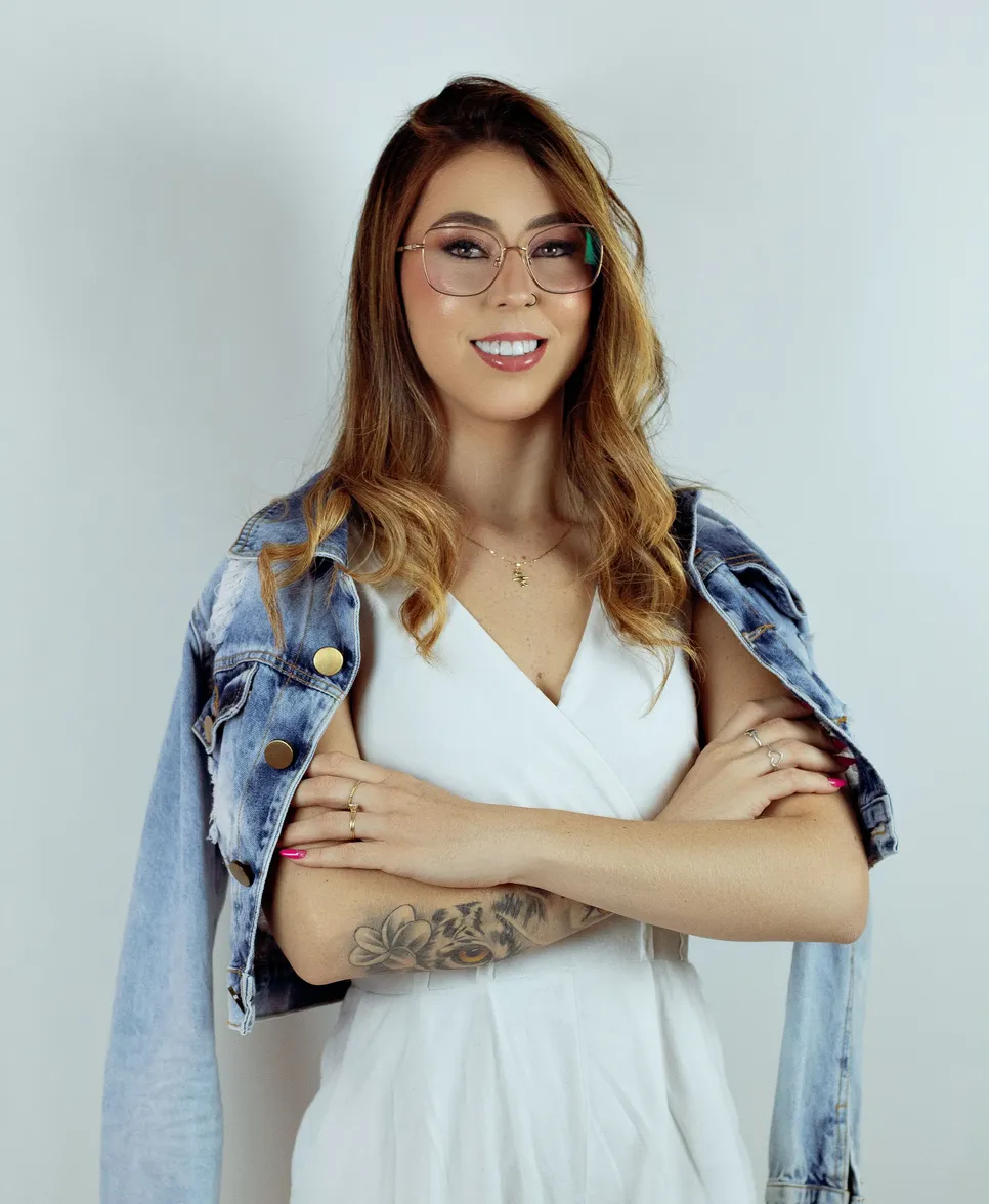 Valentina de pie con los brazos cruzados, vestido blanco y chaqueta vaquera sobre los hombros.